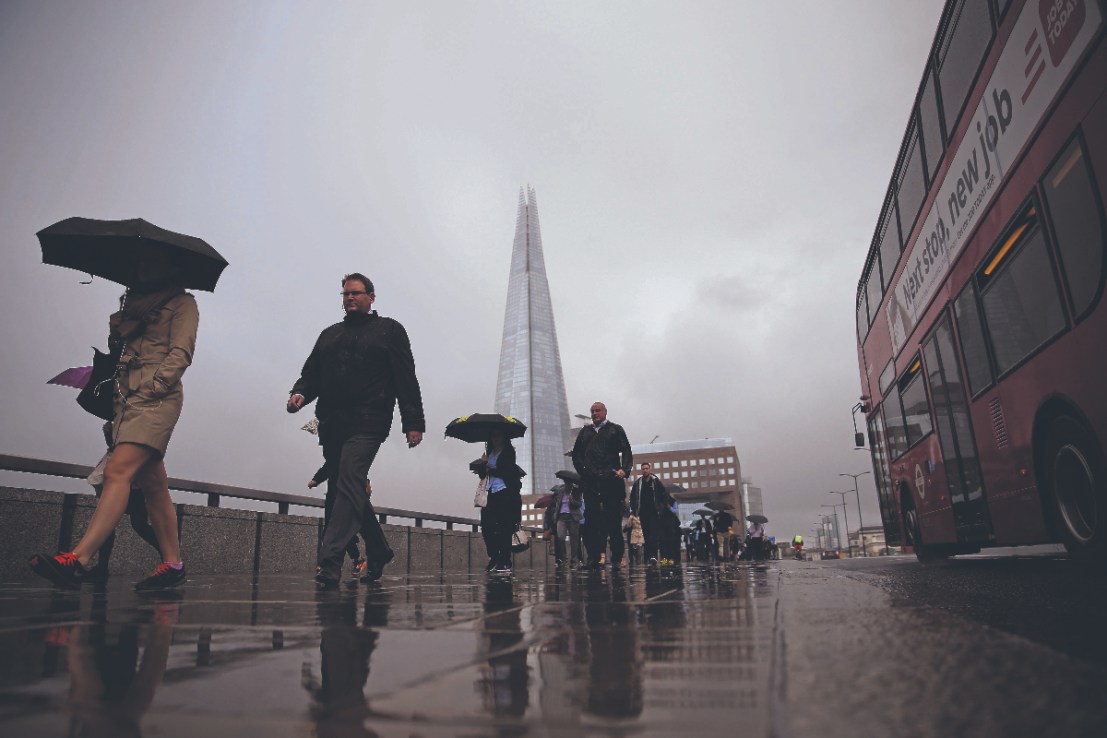 Commuters heading into the City of London walk in the rain across London Bridge, in front of the Shard skyscraper, in central London   (Photo credit should read ODD ANDERSEN/AFP/Getty Images)