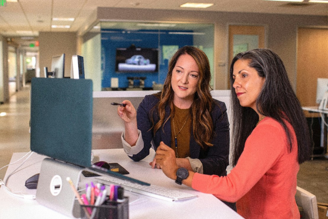 Two business women talking about sales in office at desk with laptop (Photo: Unsplash)